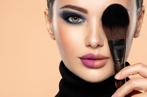 Schöne Frau mit hellem Make-up bedeckt ein Auge im Gesicht mit Make-up-Pinsel