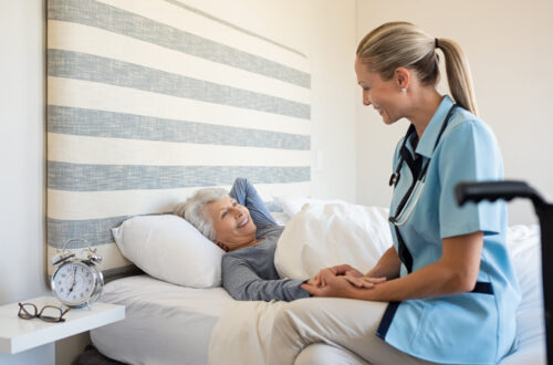 Lächelnde Krankenschwester spricht mit ihrer Patientin, einer älteren Frau, die zuhause im Bett liegt