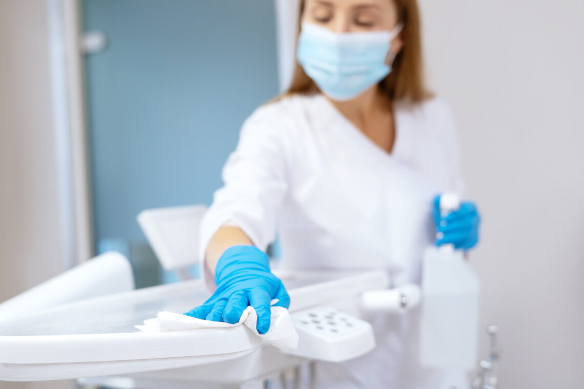 Krankenschwester in Schutzhandschuhen reinigt die Arbeitsfläche in einer Klinik mit Desinfektionstüchern